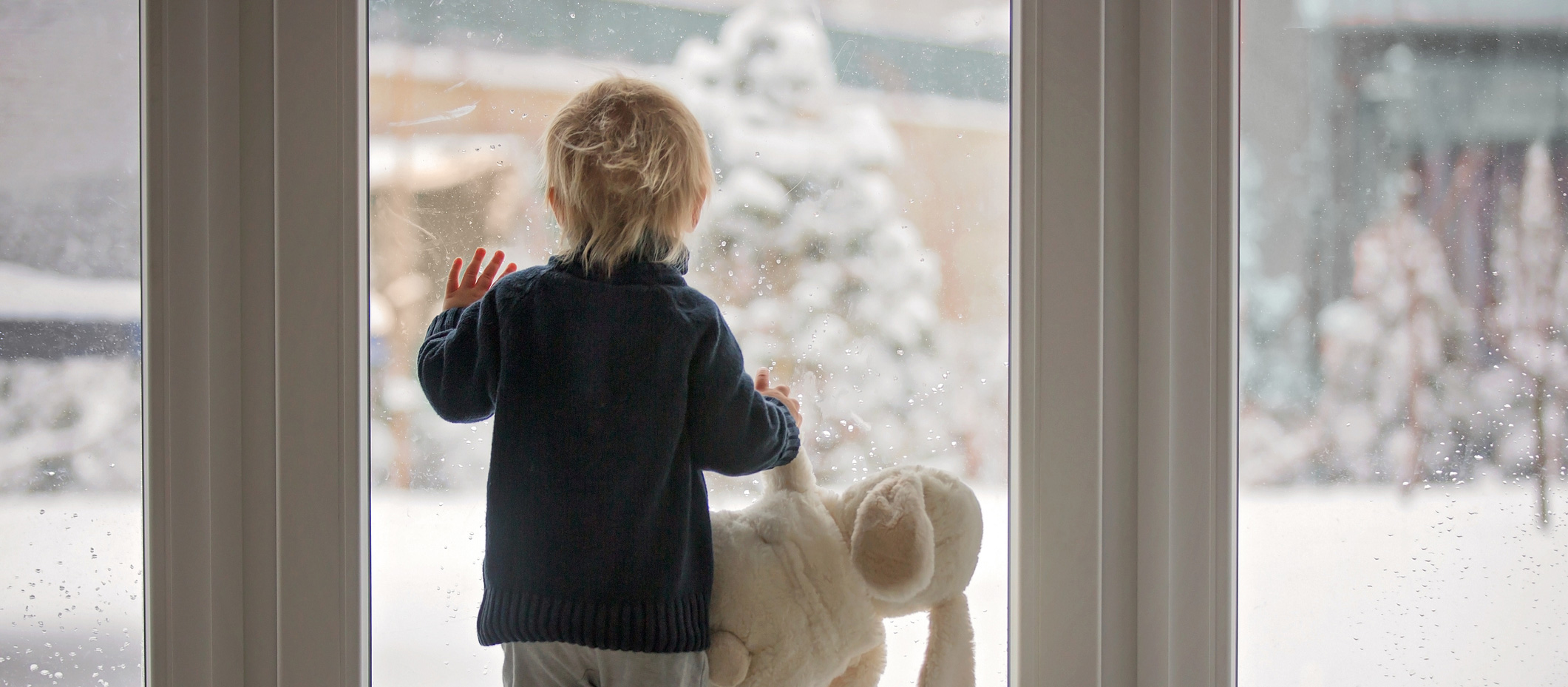 Young boy looking out back window at winter scene
